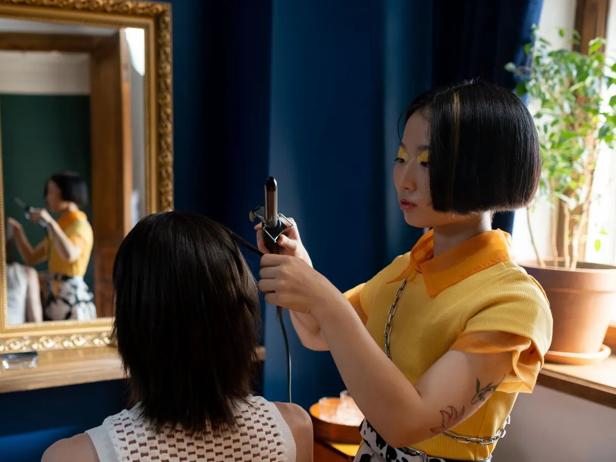 Estilista dando forma al cabello con tenaza en un salón elegante