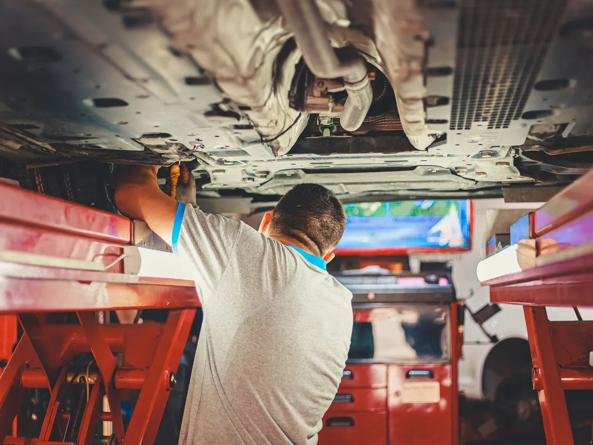 Mecánico trabajando bajo un auto levantado en la rampa hidráulica
